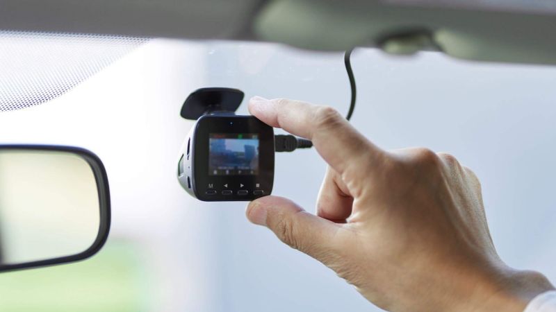 a person holding a camera in their hand that is placed as a dashcam in a car