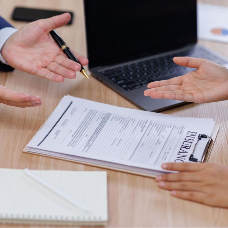 Two people discussing an insurance contract at a desk with a laptop and documents.