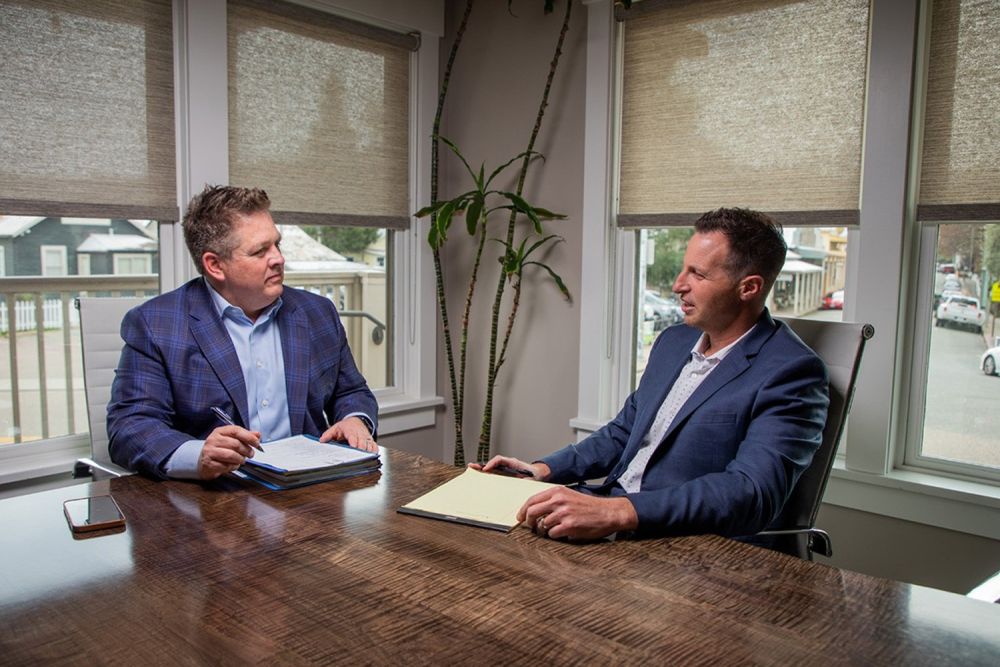 Attorneys from Redkey Gordon Law, wearing suits, are having a meeting at a conference table near bright windows.