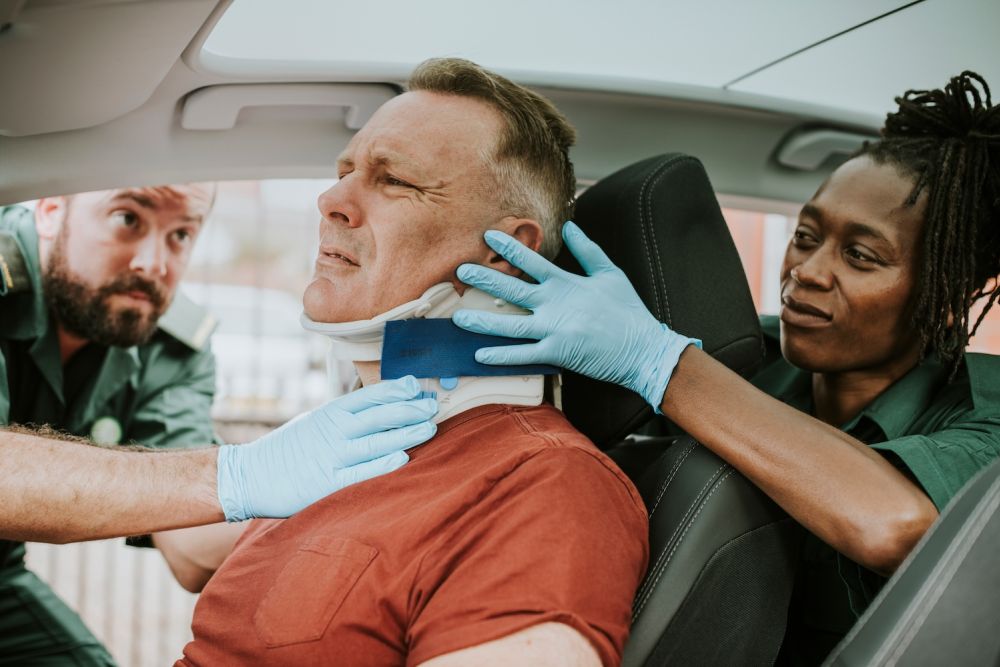 Paramedics applying neck brace to injured man in car accident scene.