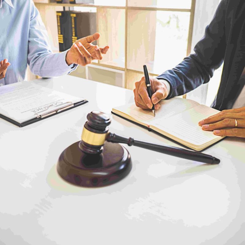 Law consultation in office with a gavel, documents, and two people discussing legal matters.