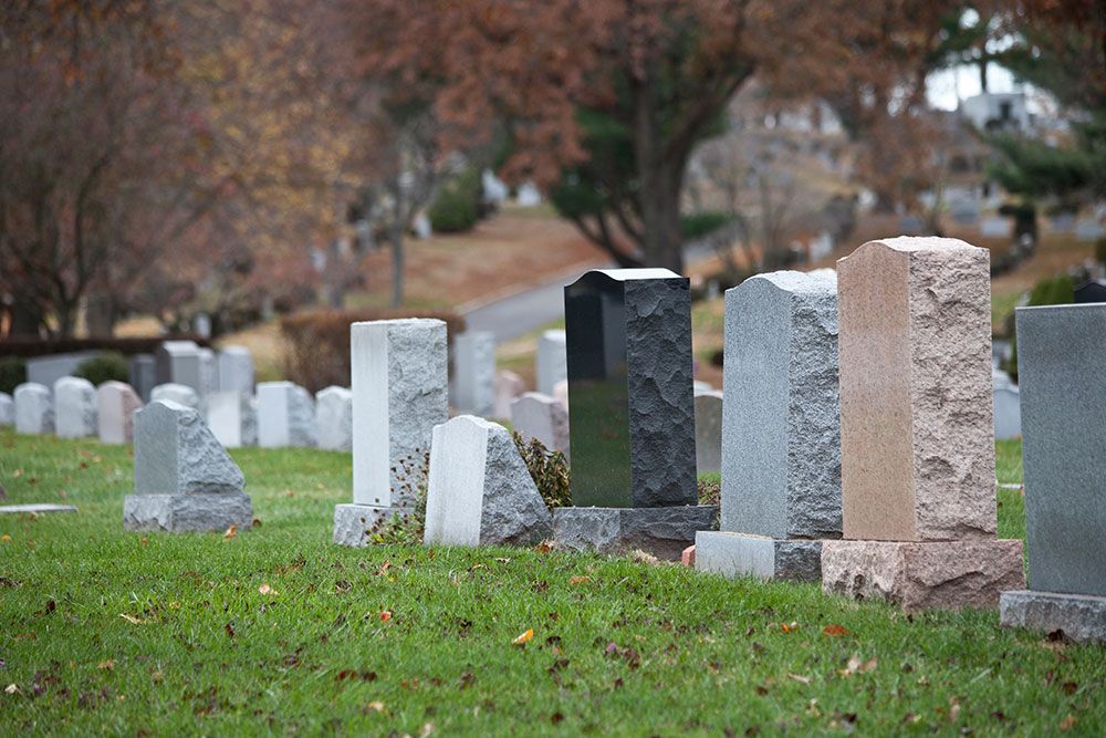 Gravestones in a serene cemetery on a fall day, surrounded by lush grass and autumn trees.