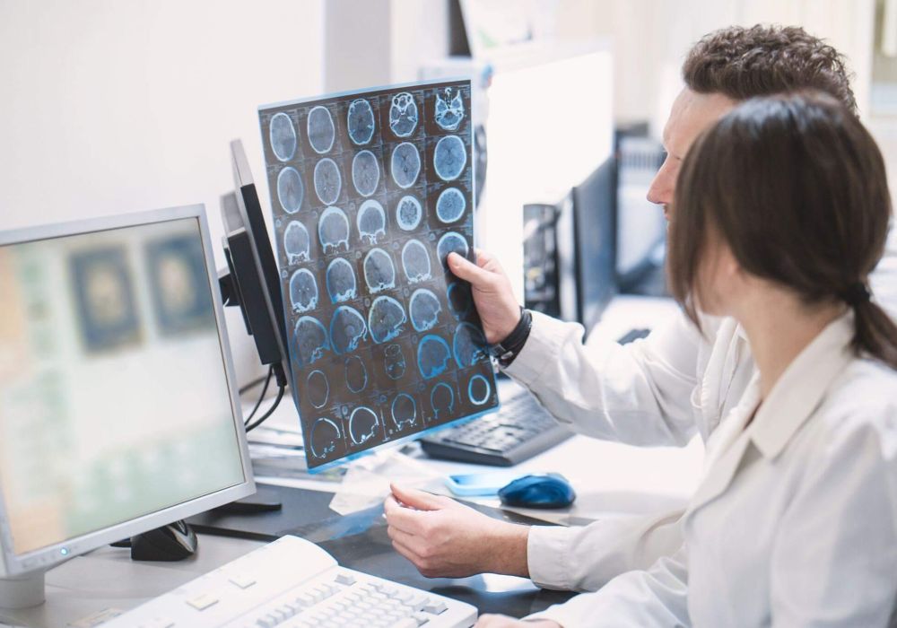 a woman sitting at a desk with a computer and reviewing an x-ray