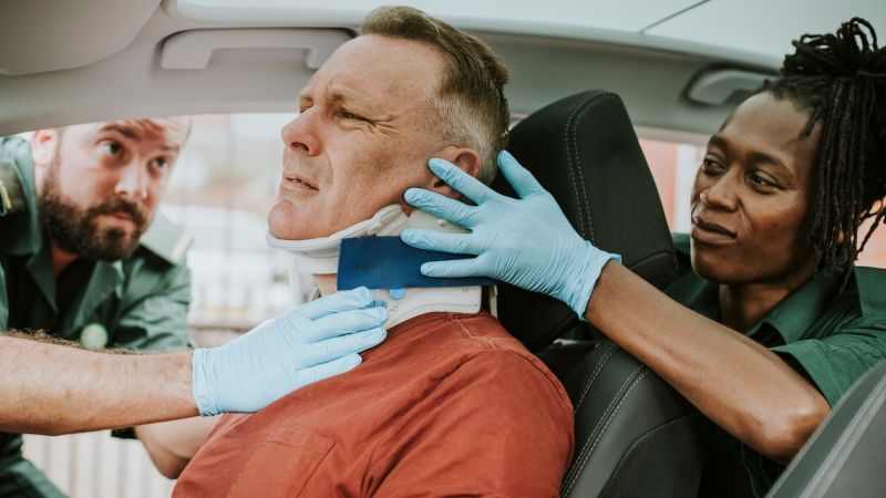 Paramedics applying neck brace to injured man in car accident scene.