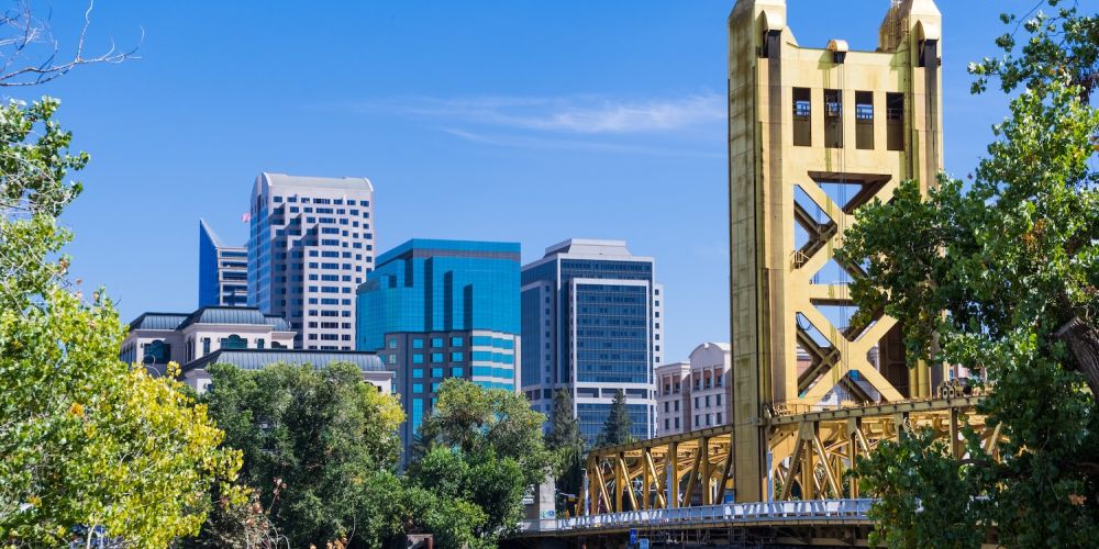 Golden Tower Bridge and downtown Sacramento skyline under a clear blue sky.