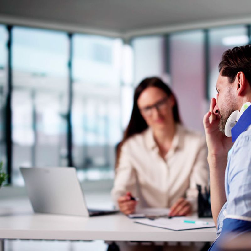 Man with neck brace consulting female professional in modern office setting.