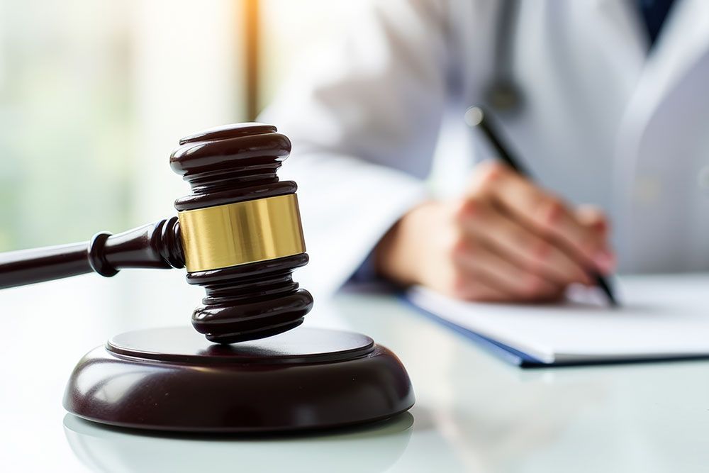 Judge's gavel on desk with person writing, symbolizing legal consultation or decision-making.