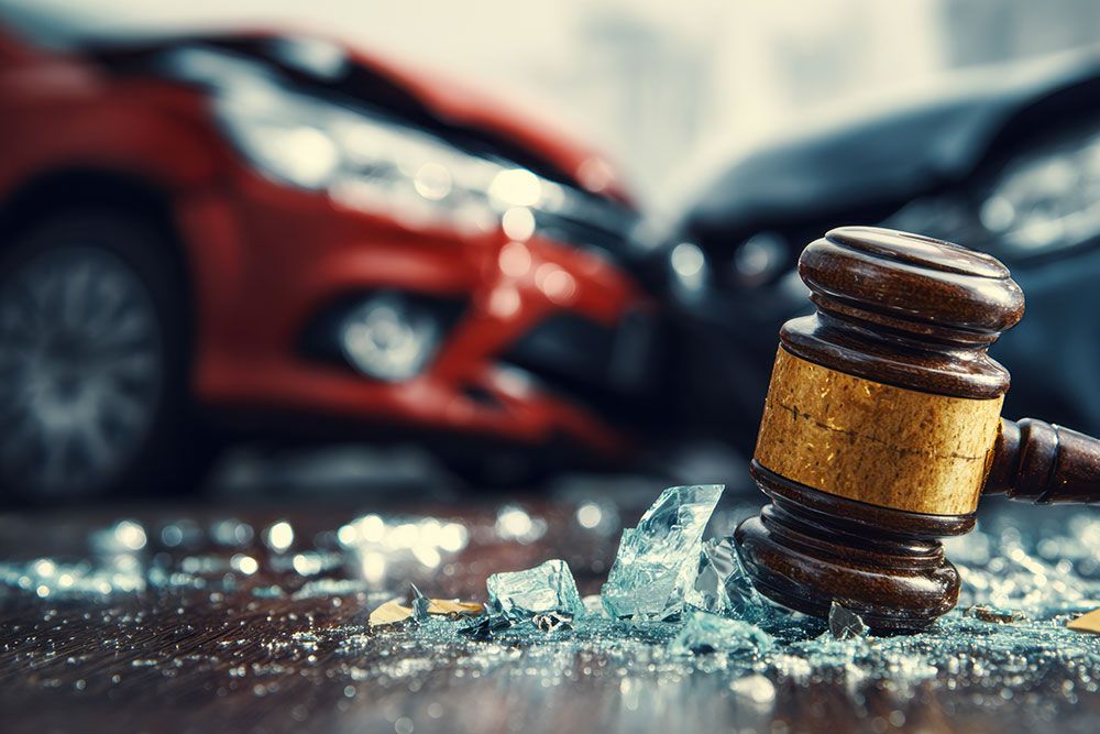 Gavel with broken glass and a car crash in the background, symbolizing legal action in auto accidents.