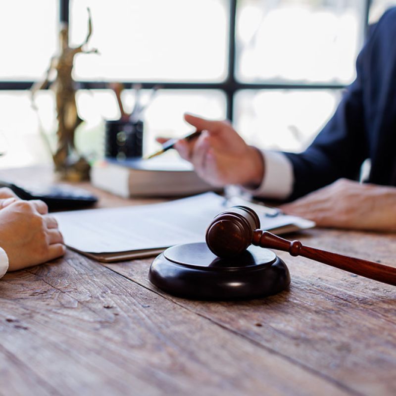 Lawyer consulting with client at desk, gavel and legal scales visible, symbolizing justice and legal advice.