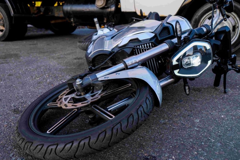 Motorcycle lying on the road after an accident, showing front wheel and headlight for close-up detail.