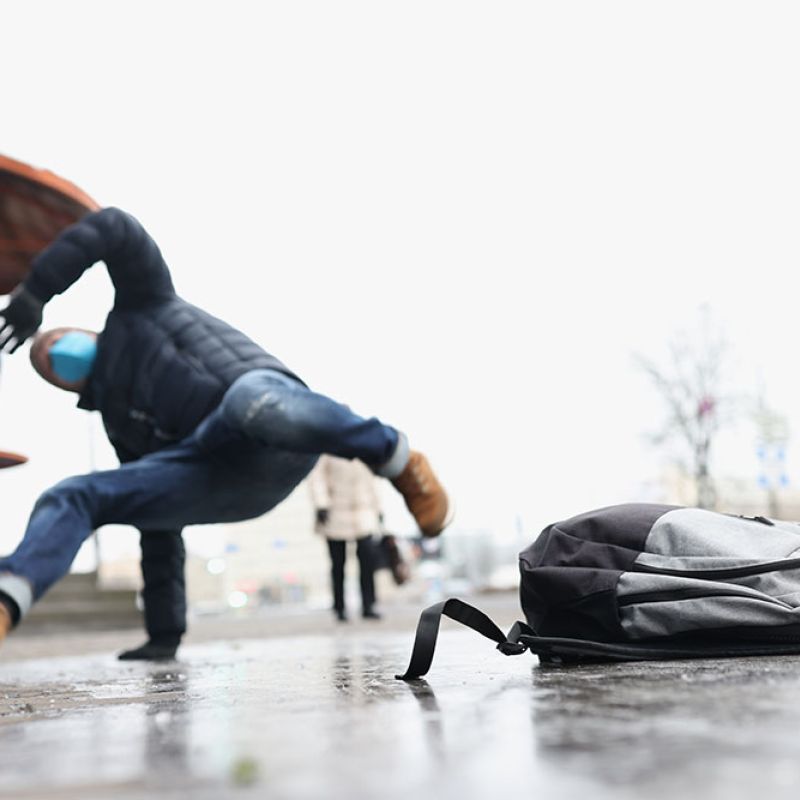 Man slipping on icy sidewalk near a backpack in winter street.