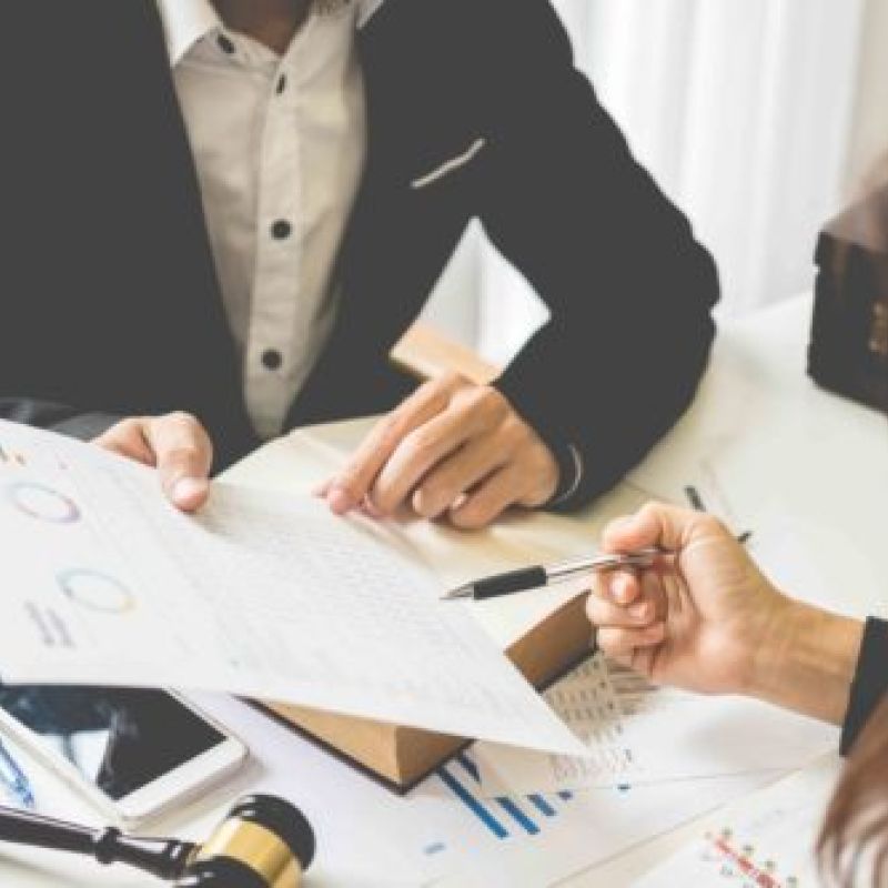Two professionals discussing financial documents at a desk, reviewing charts and data with a gavel in view.