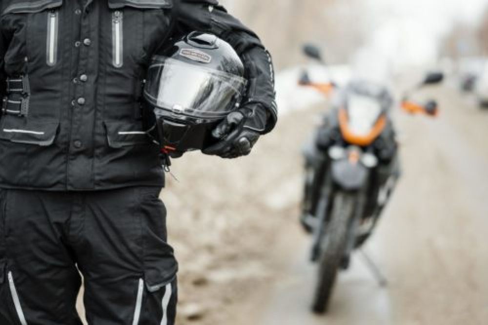 Motorcyclist holding helmet, standing near parked sport bike on a rural road, showcasing safety gear and adventure.