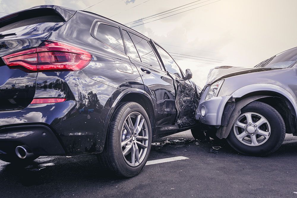 Two cars in a collision on a road, with visible damage to the vehicles' front and side area.