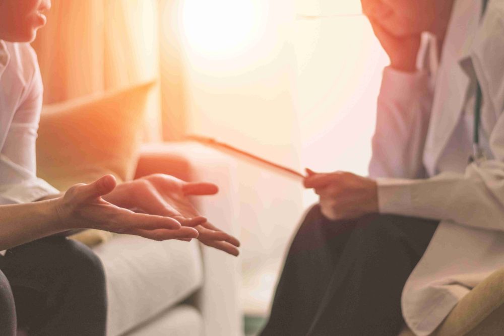 Person gesturing during a consultation with a doctor on a couch, highlighting communication and health discussion.