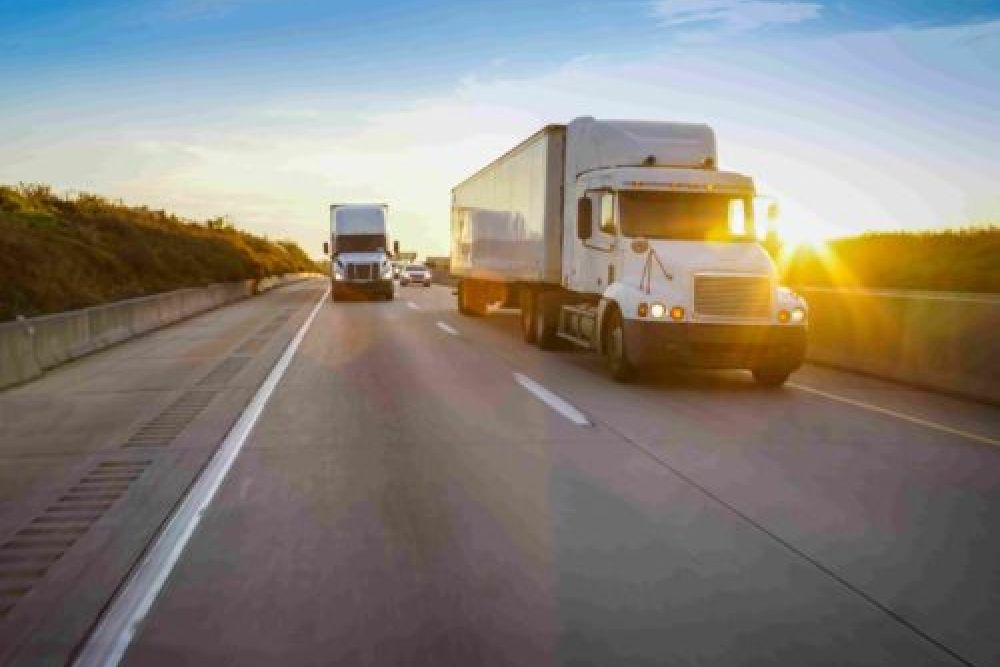 Two semi-trucks driving on a highway at sunrise, showcasing transportation and logistics in motion.