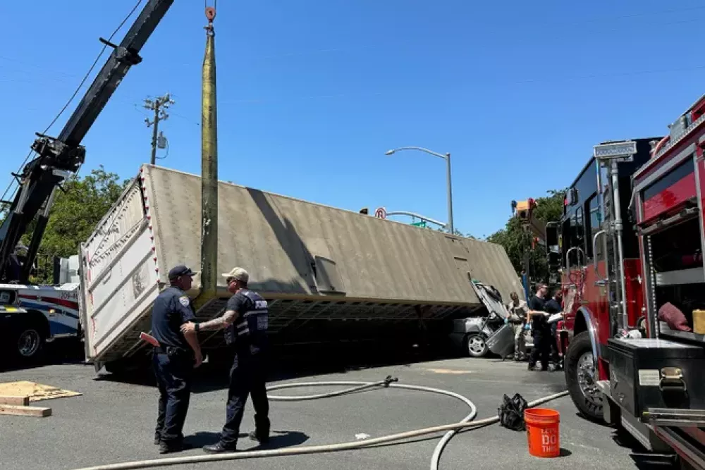 Emergency personnel respond to overturned semi-truck accident with crane and fire truck assistance.