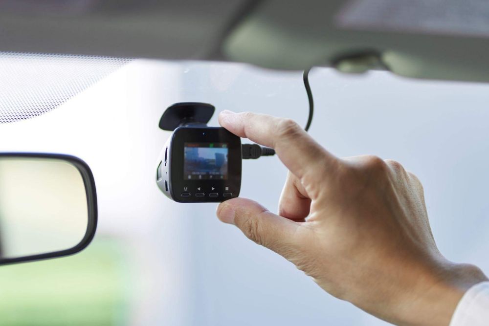 a person holding a camera in their hand that is placed as a dashcam in a car