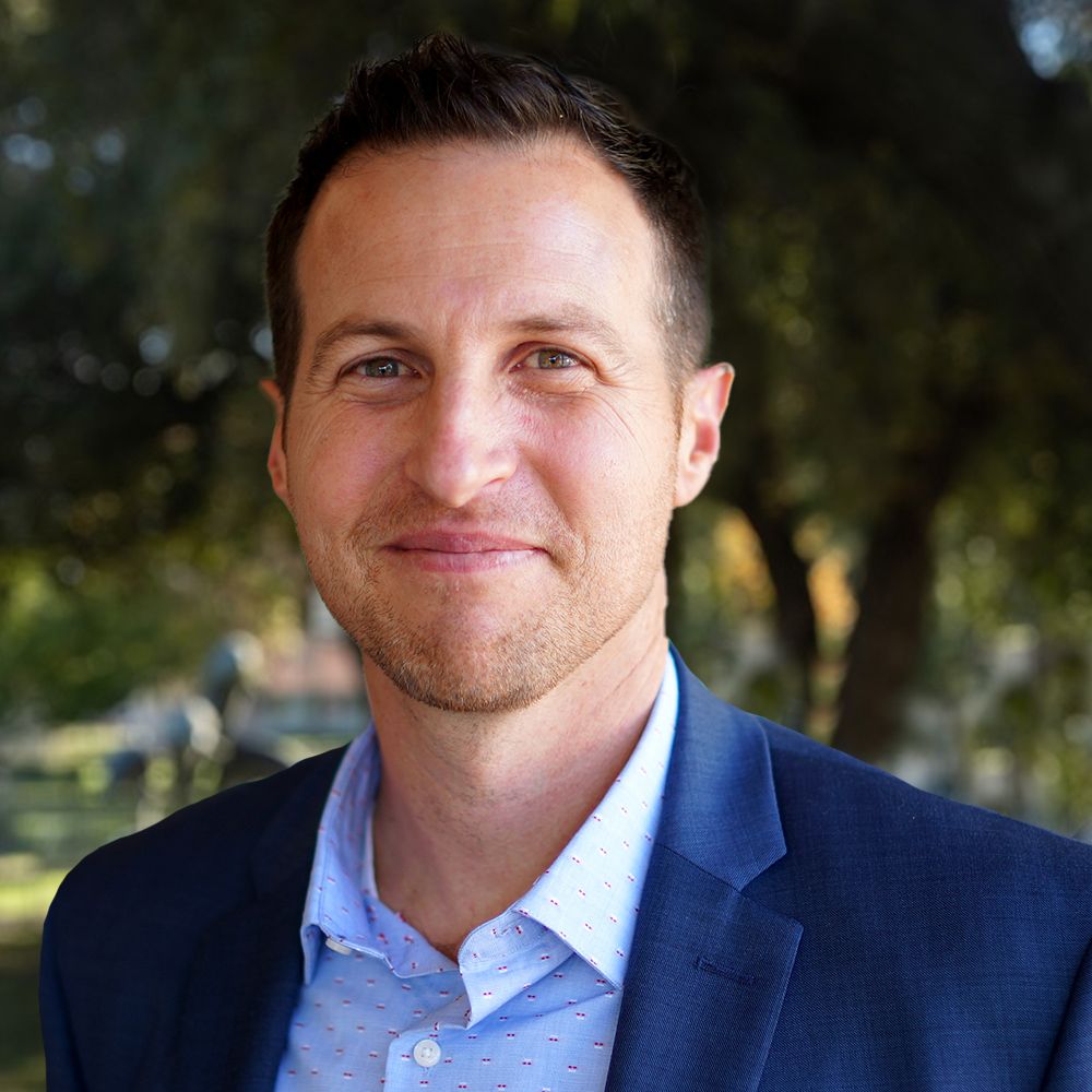 Robert Gordon in blue blazer outdoors, standing in a park with trees in the background.