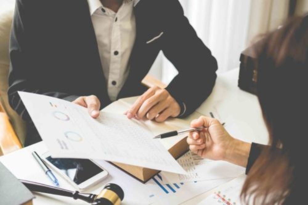 Two professionals discussing financial documents at a desk, reviewing charts and data with a gavel in view.