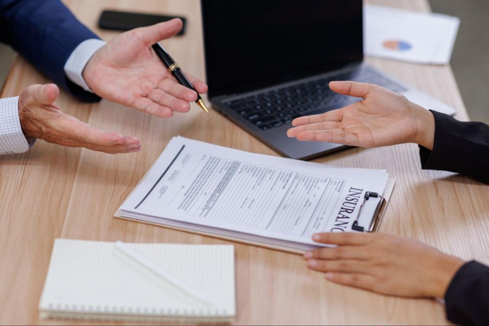 Two people discussing an insurance contract at a desk with a laptop and documents.