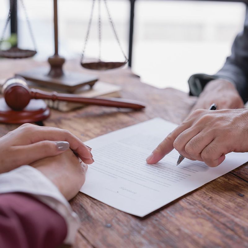 Legal consultation with documents, gavel, and scales on a wooden desk. Attorney advising client, emphasizing agreement details.
