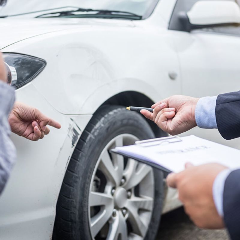Insurance agent evaluating car damage with a man pointing at a white vehicle's scratched bumper.