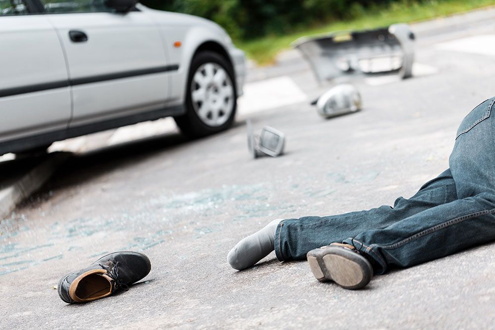 Car accident scene with debris and injured person on road, depicting vehicle collision aftermath.