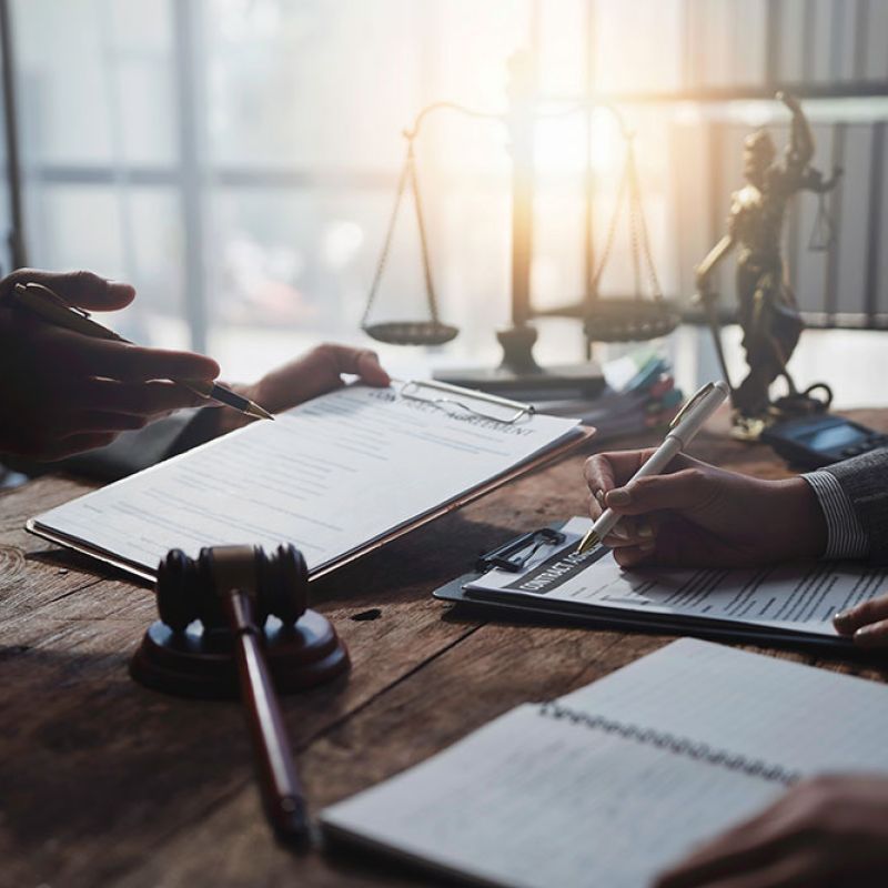 Legal team discussing documents at office table with gavel and scales of justice in background.
