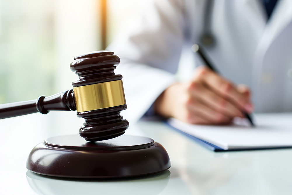 Judge's gavel on desk with person writing, symbolizing legal consultation or decision-making.