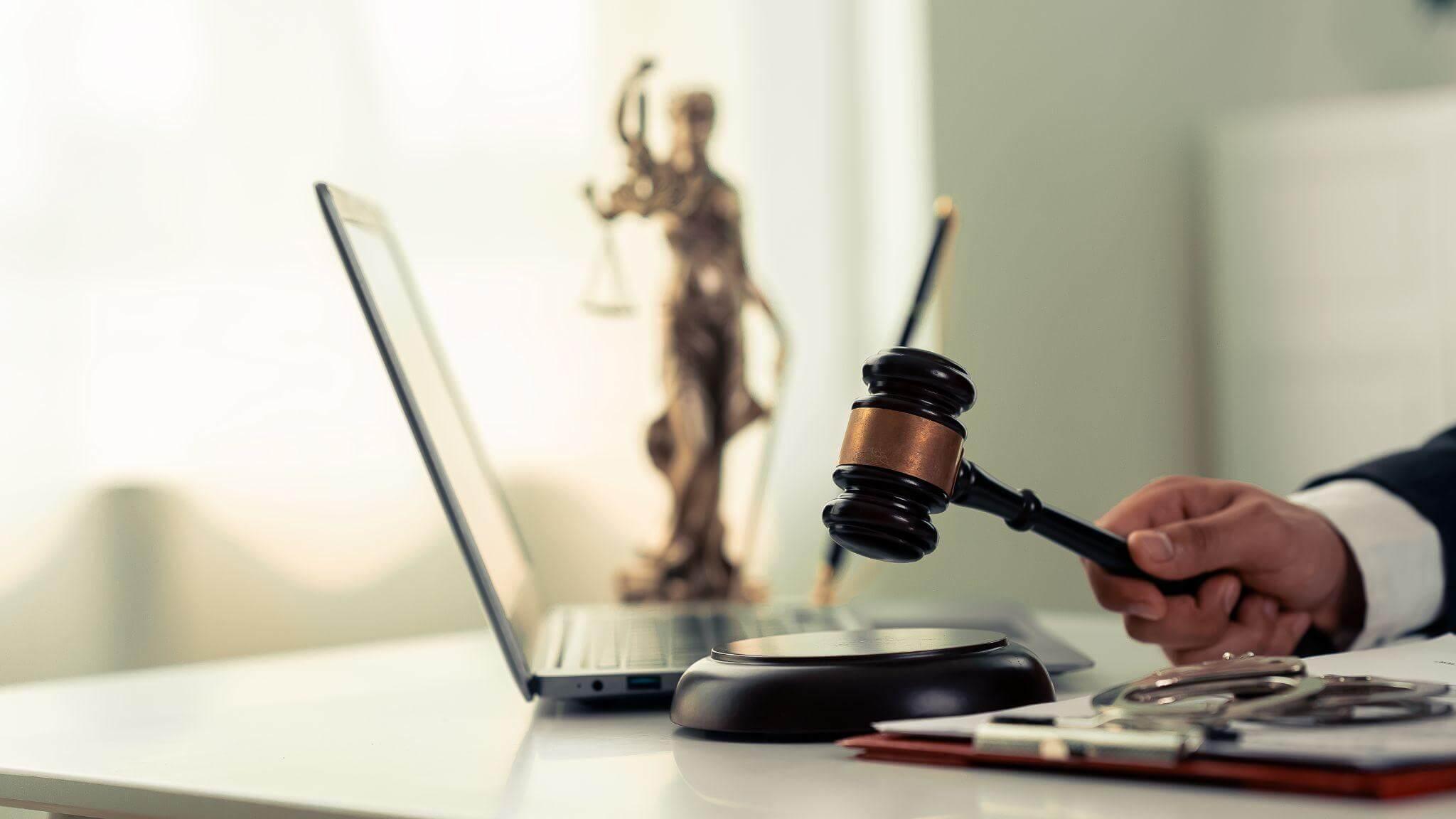 a judge holding a gavel in front of a laptop as if dictating sentence