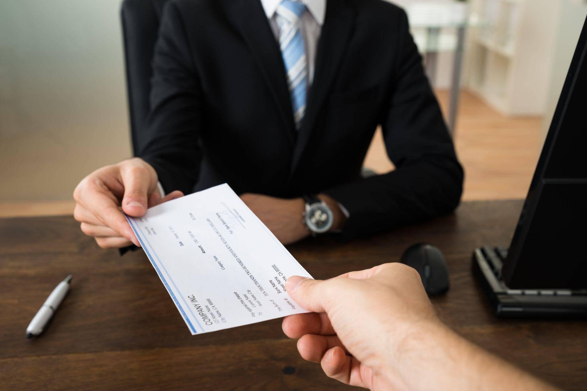 a man in a suit handing a check to another man in what appears to be a formal environment