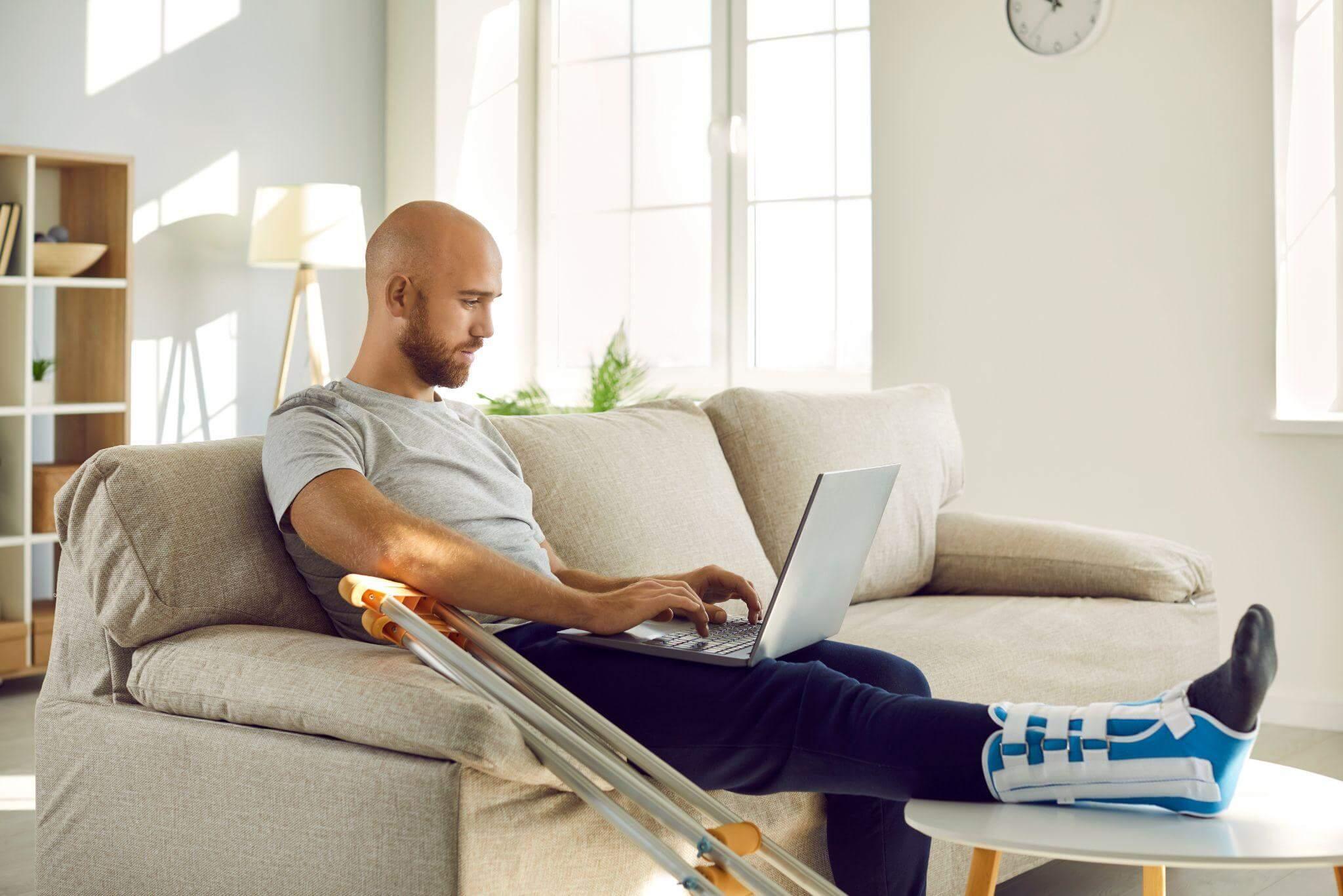 a man sitting on a couch using a laptop computer, the man is injured but recovering