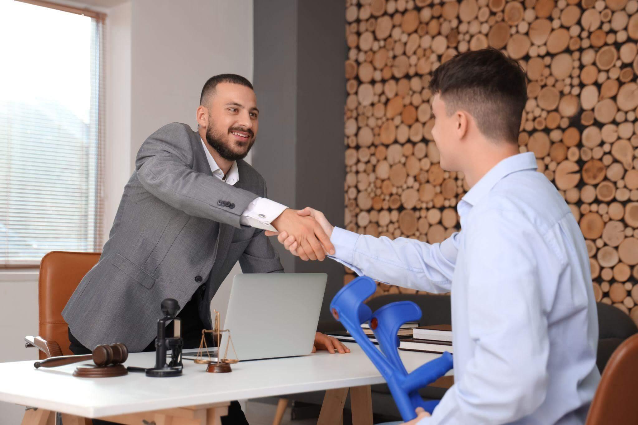 two men shaking hands in front of a laptop in an attorney's office