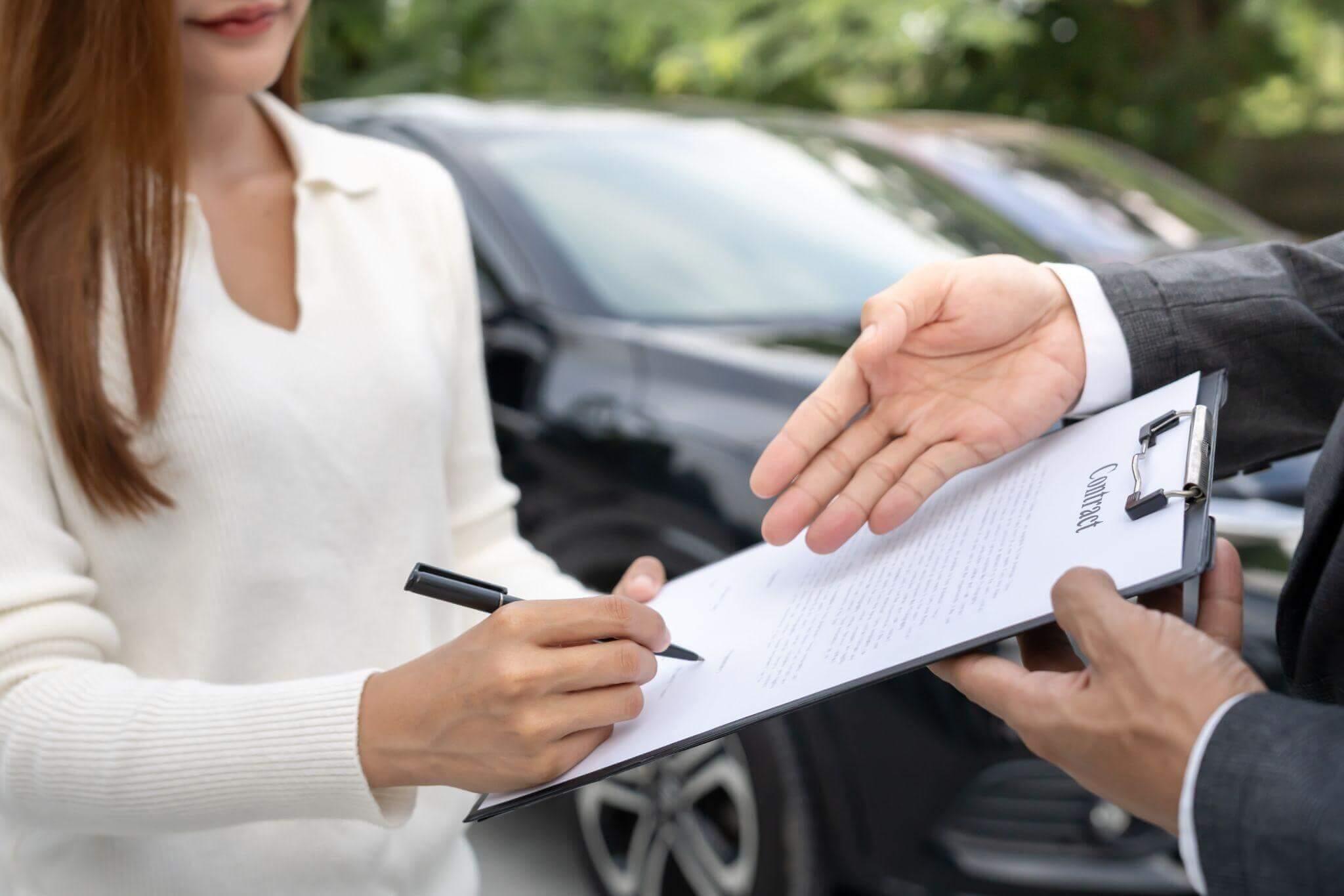 A woman signs a document titled "Contract" on a clipboard held by a suited individual, standing near a black car in an outdoor setting.