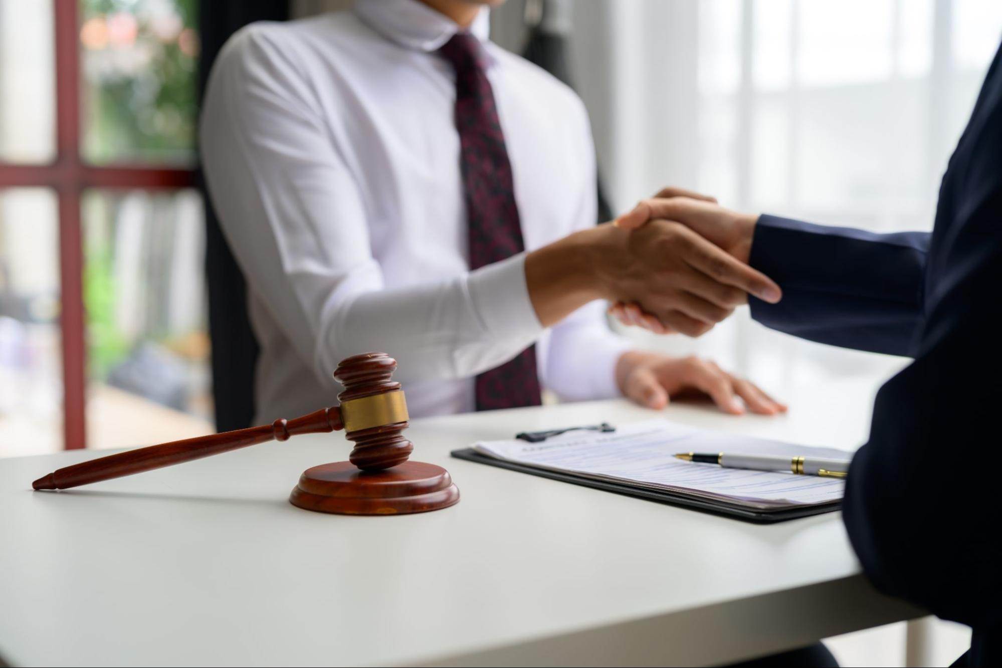 Lawyer handshake agreement with gavel and contract on table, symbolizing legal partnership and contract signing.