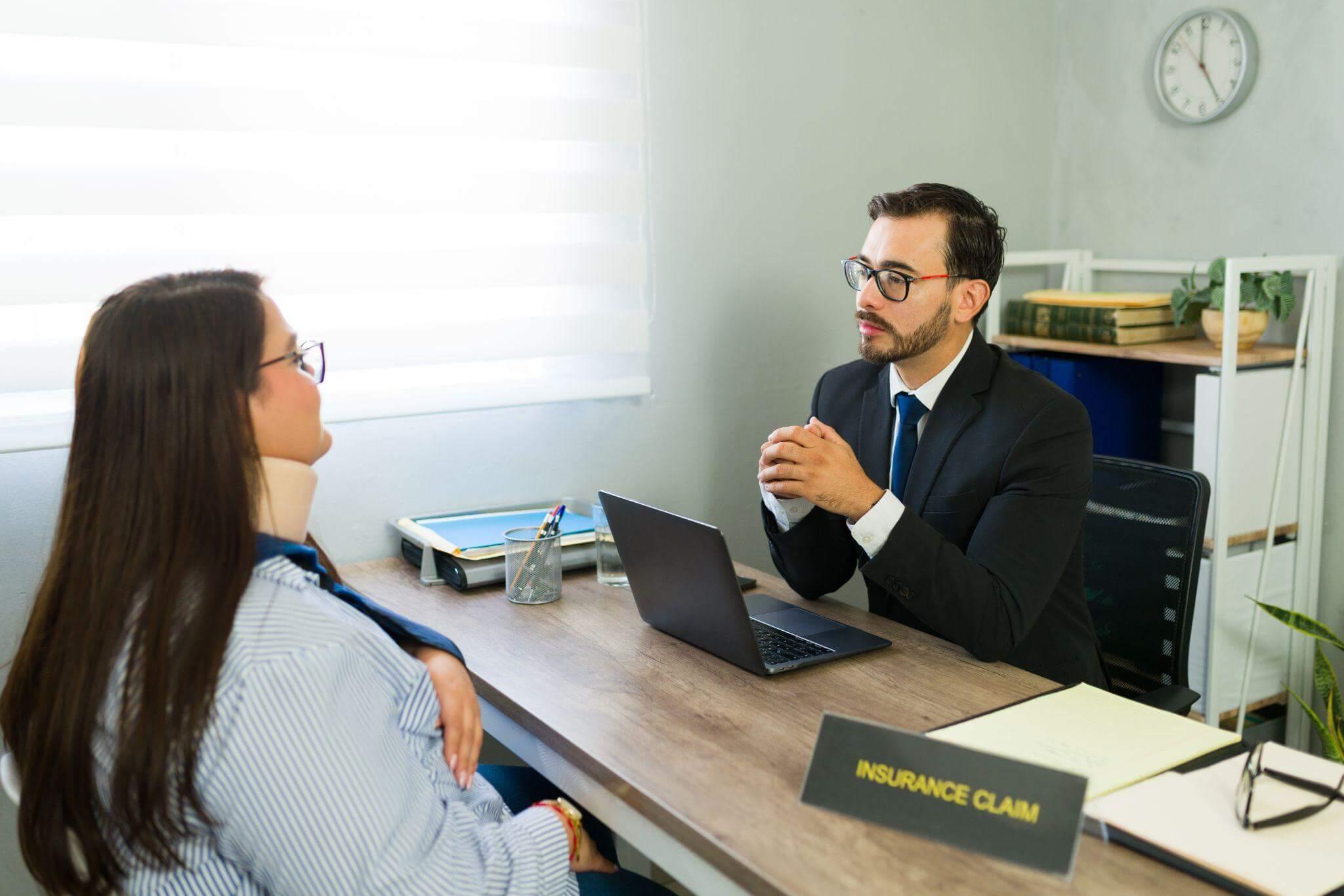 a man and a woman sitting at a desk with a computer and papers, there's a label that reads "insurance claim"