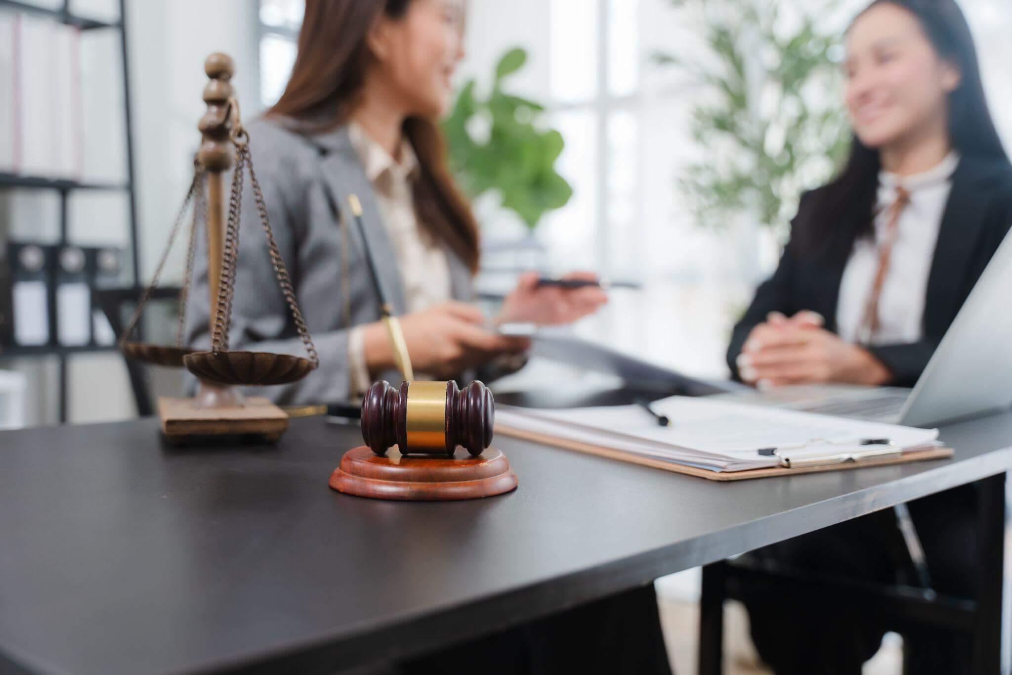 Two women discuss a legal case with a scale of