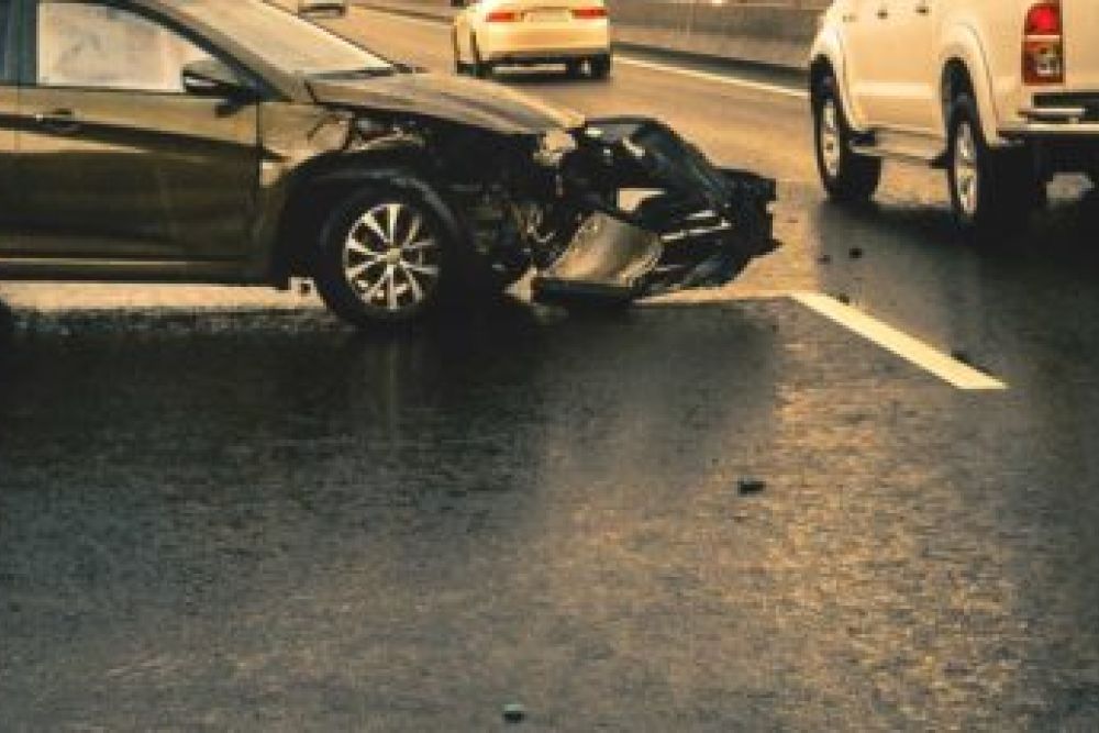 Car accident scene on a highway, showing two vehicles with significant damage on a rainy day.
