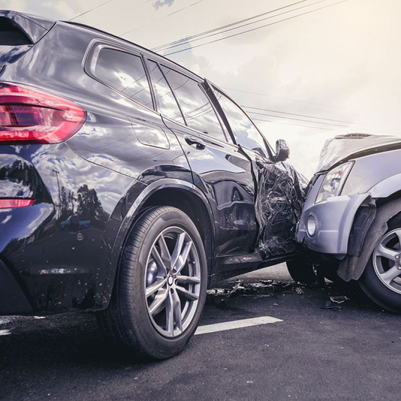 Two cars in a collision on a road, with visible damage to the vehicles' front and side area.