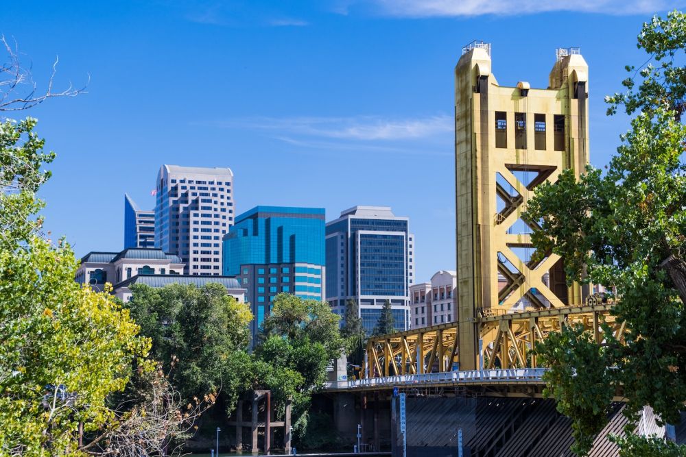 Golden Tower Bridge and downtown Sacramento skyline under a clear blue sky.